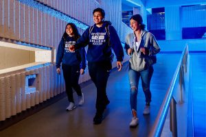 Three students walk down indoor Main Campus ramp.